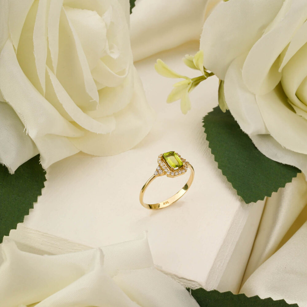 Peridot 14K gold ring with emerald-cut green gemstone displayed among white roses.
