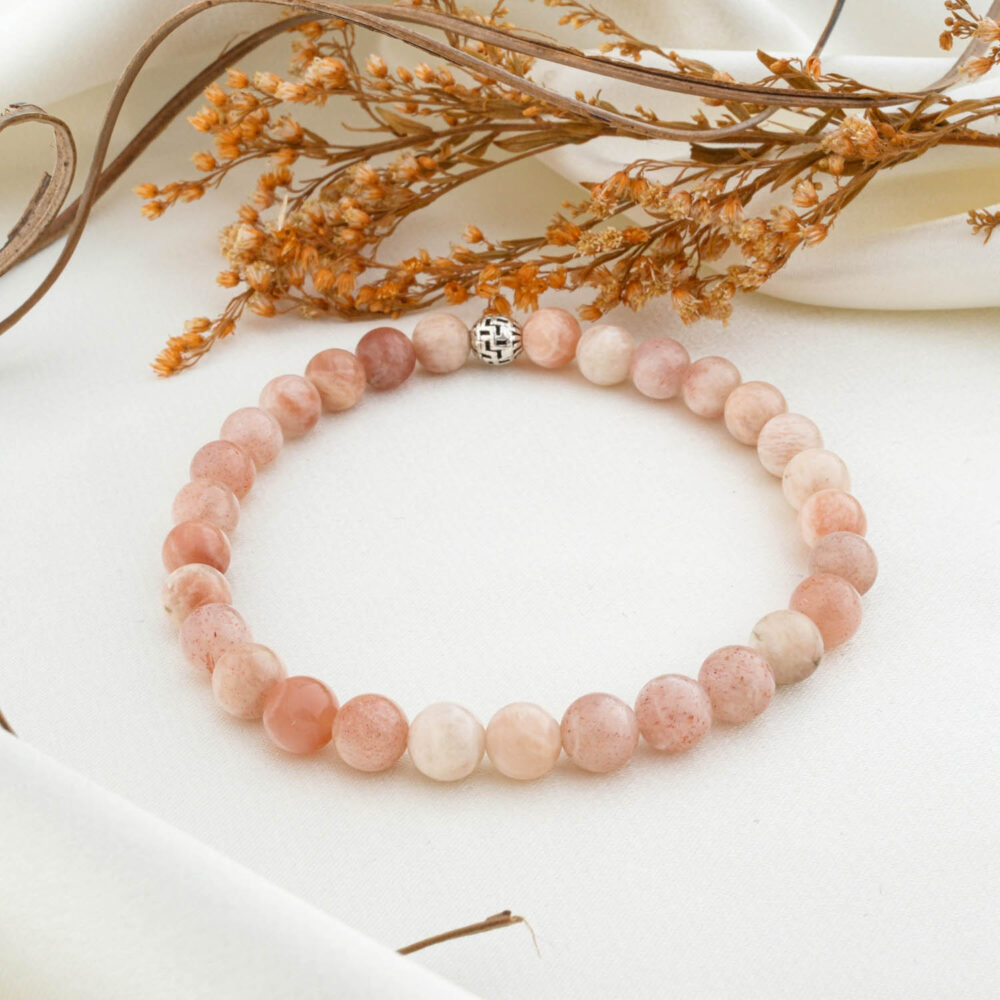 A 2A+ quality 6mm natural sunstone beaded bracelet with a silver clasp, on a white silk fabric.