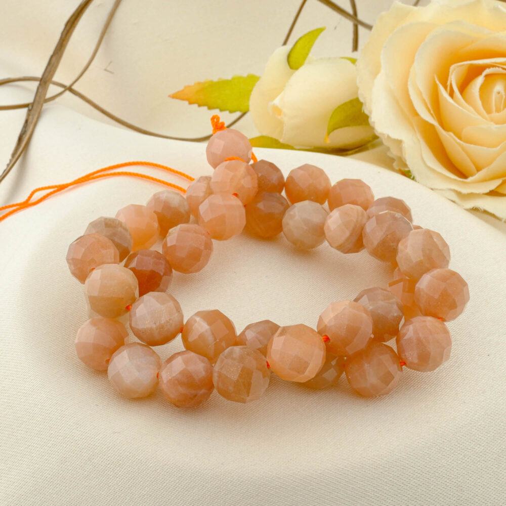 A double-wrapped strand of 10mm 4A+ quality faceted sunstone beads with a sparkling peach-orange color on a cream fabric.