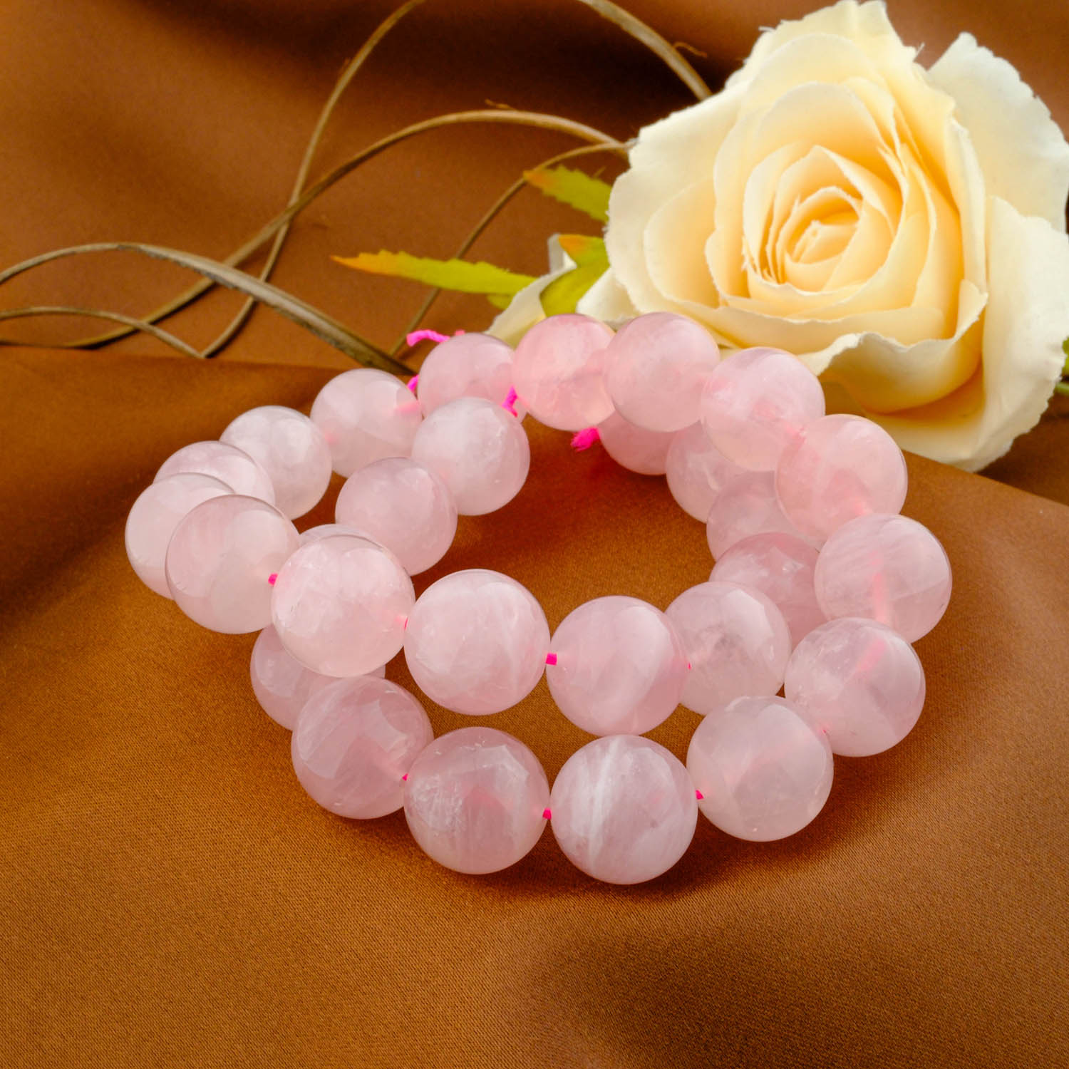 5a-madagascar-rose-quartz-beads-14mm A double-wrapped strand of 5A+ quality 14mm natural rose quartz beads with a soft, gentle pink color on a brown fabric.