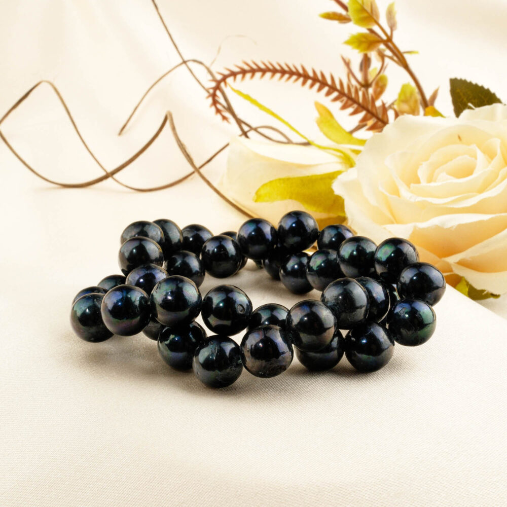 Strand of large near-round black saltwater pearls, 10-11mm average size, displayed on cream satin near roses.