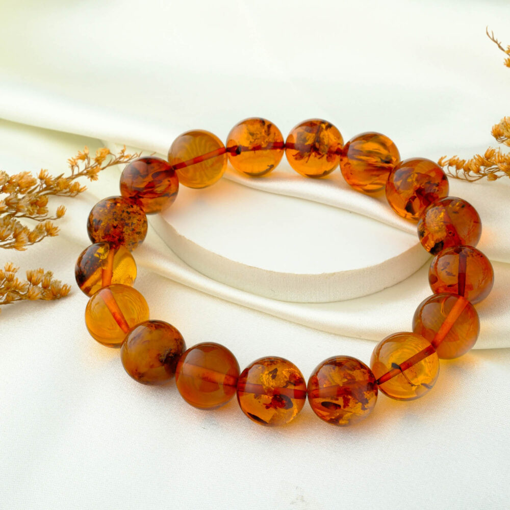 Certified amber bead bracelet with 12–13 mm round beads on neutral fabric