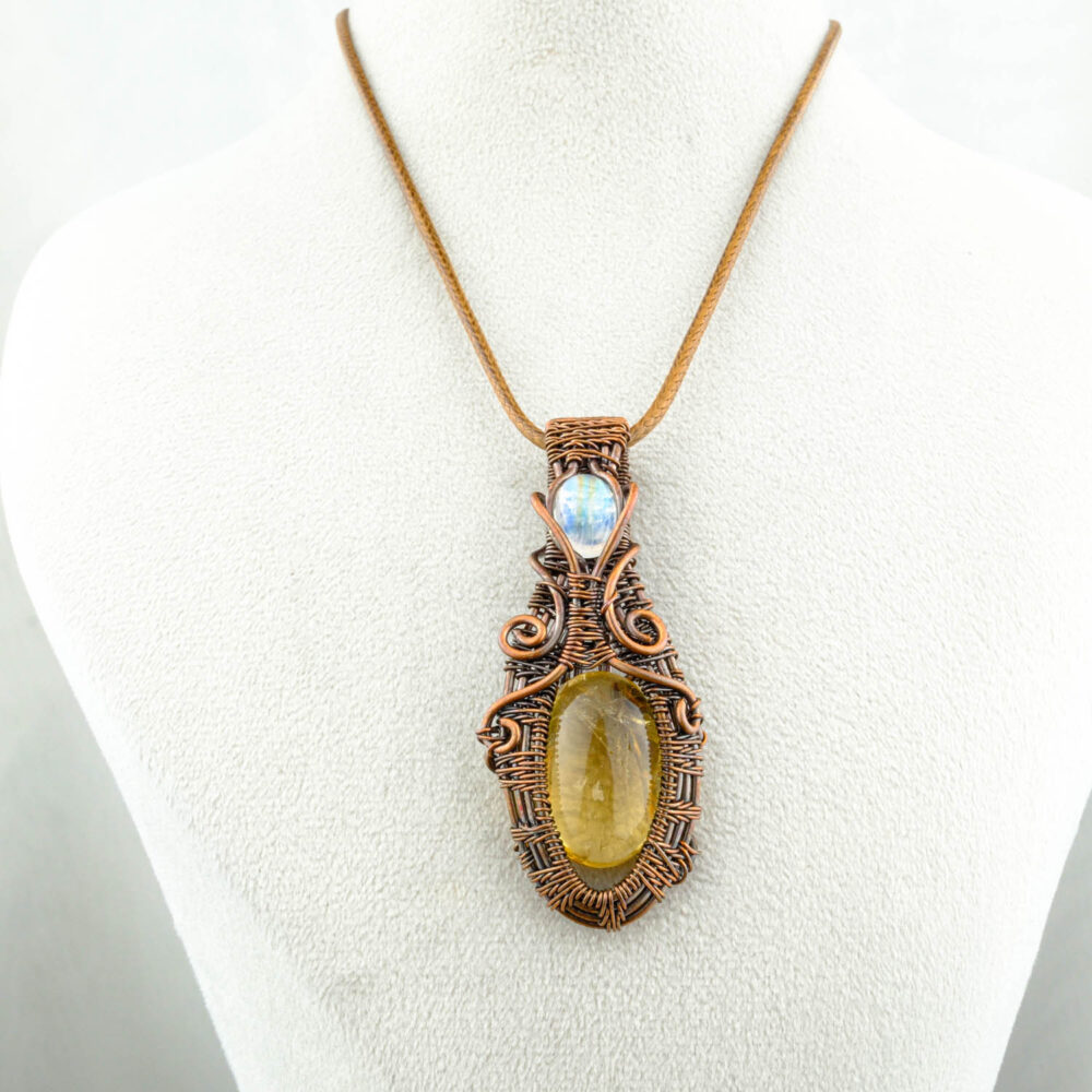 Colgante artesanal de citrino y piedra luna con alambrado de cobre sobre fondo satinado
