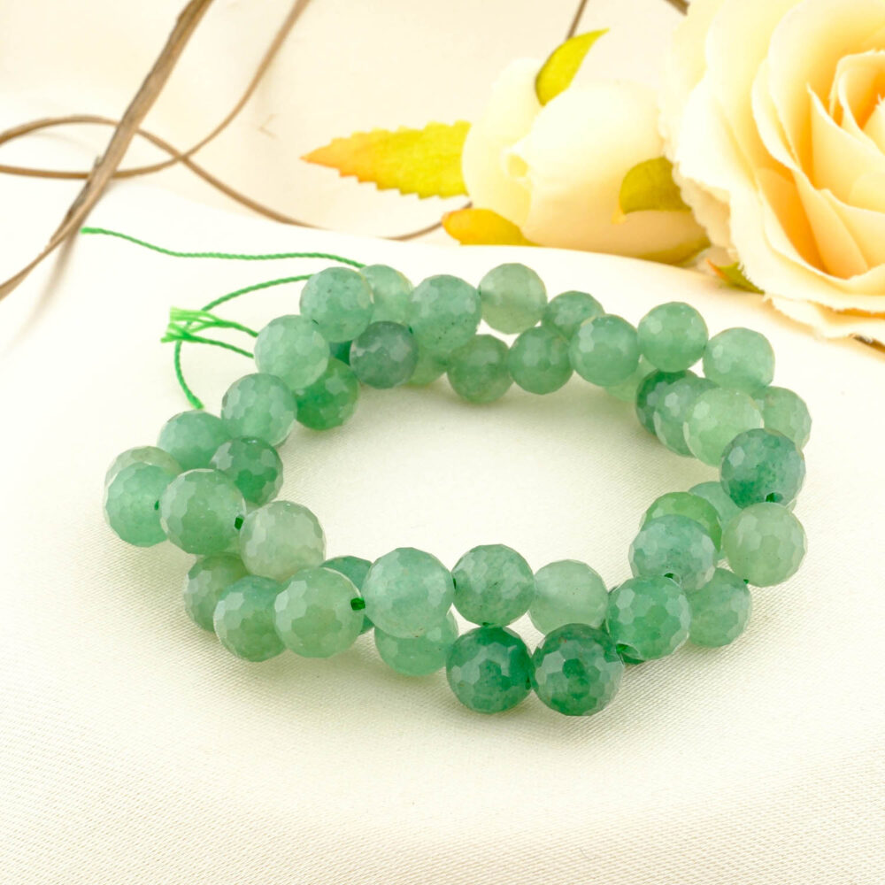 A double-wrapped strand of 8mm faceted green aventurine beads with a vibrant, gentle green color on a cream fabric.