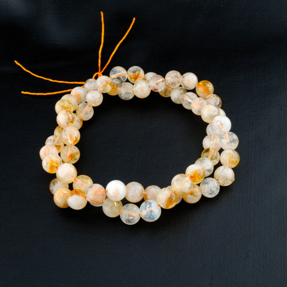 Hebra de cuentas de citrino natural de 6mm, con inclusiones y tonos amarillo-naranja, sobre un fondo marrón con una rosa.