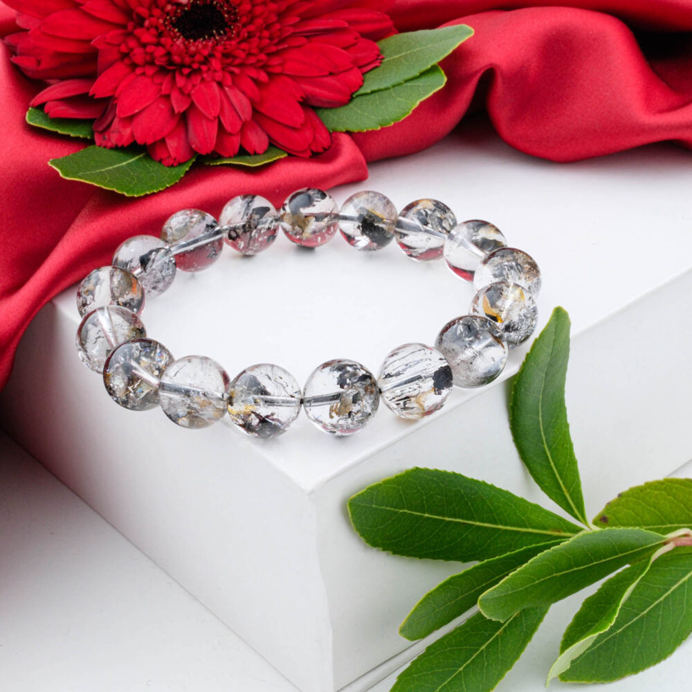 A 12-13mm Herkimer Diamond bracelet with clear beads and black anthraxolite inclusions, shown on a white box.