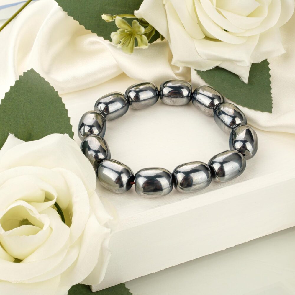 Large Terahertz stone bracelet with metallic grey capsule-shaped beads, shown on a white box near white roses.