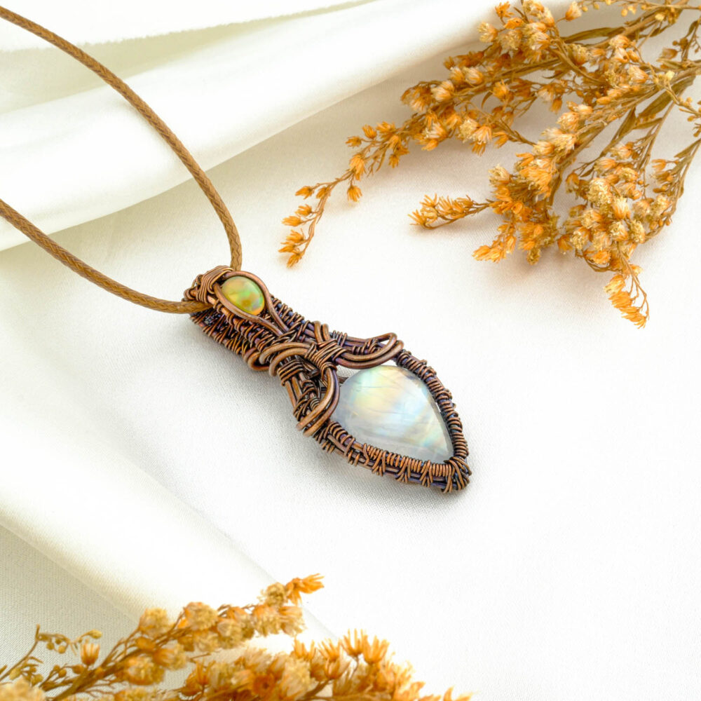 Handmade moonstone and opal copper wire-wrapped pendant on satin backdrop