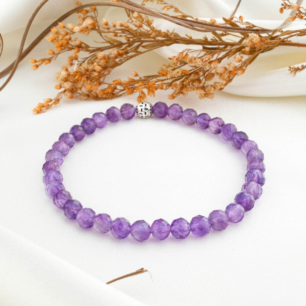 A natural 6mm amethyst beaded bracelet with a silver clasp, on a white silk fabric.