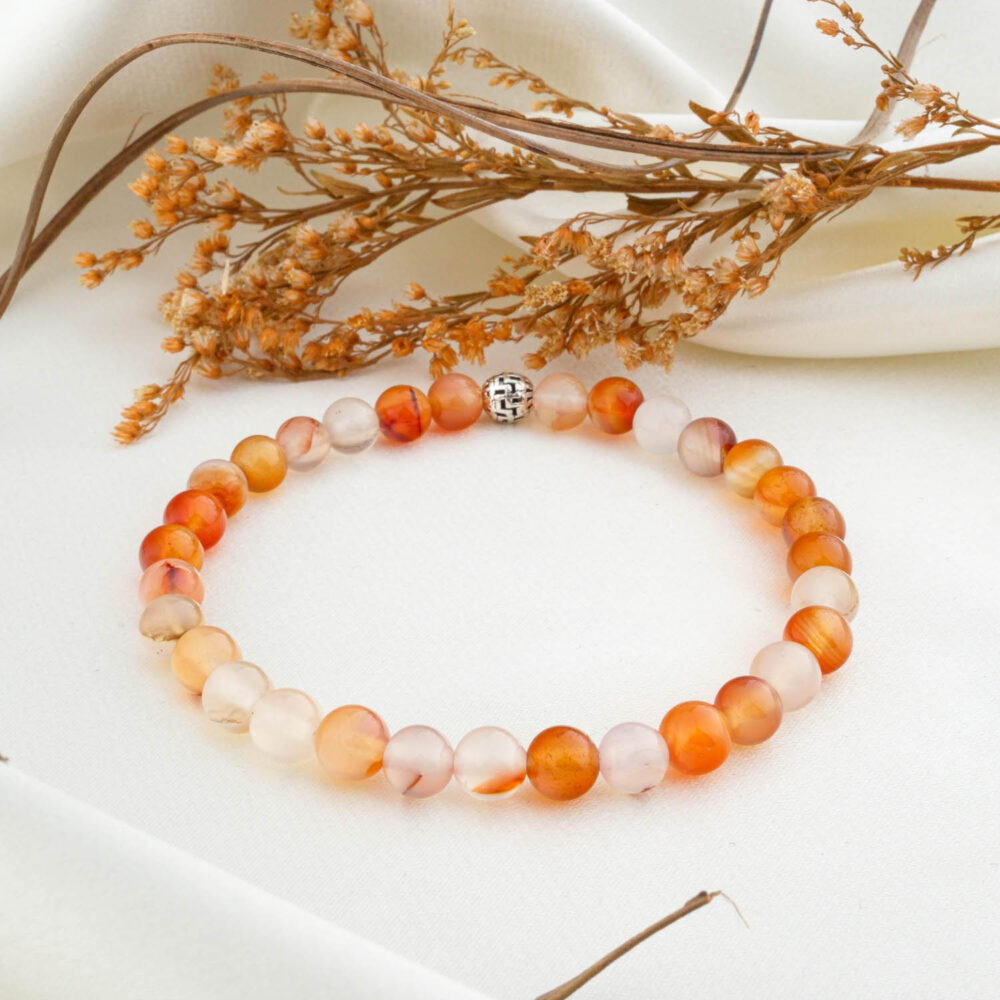 A natural 6mm carnelian agate beaded bracelet with a silver clasp, on a white silk fabric.