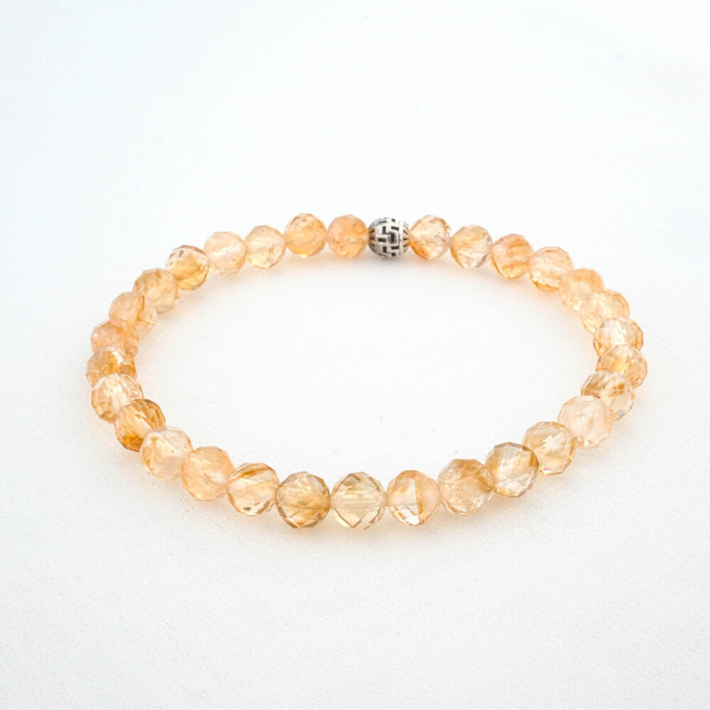 Close-up of a 6mm faceted citrine bracelet showing its golden-yellow color, on a white background with dried flowers.