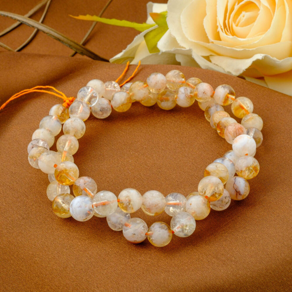 A double-wrapped strand of 6mm natural citrine beads with cloudy inclusions and yellow-orange tones on a brown fabric.
