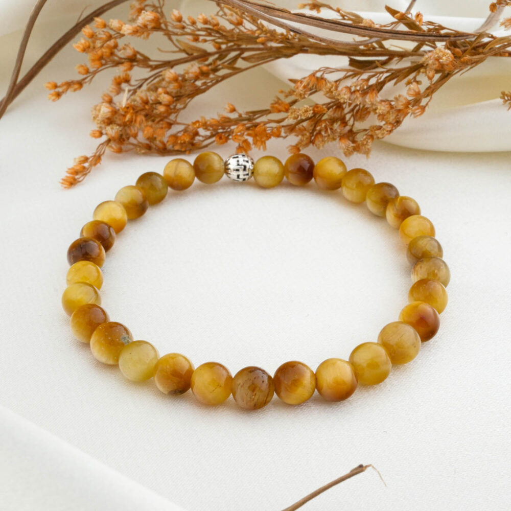 A natural 6mm yellow tiger's eye beaded bracelet with a silver clasp, on a white silk fabric.