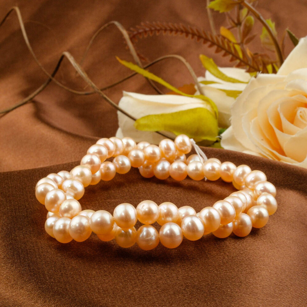 Strand of near-round rose-pink saltwater pearls, approx. 5-6mm average size, displayed on brown satin near roses.