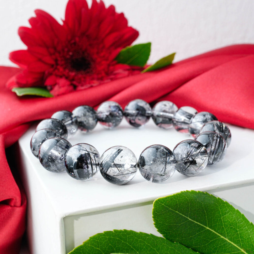 A Silver Sheen Obsidian bracelet with faceted, grey, tile-like beads in a Rolex-style design, on a white box.