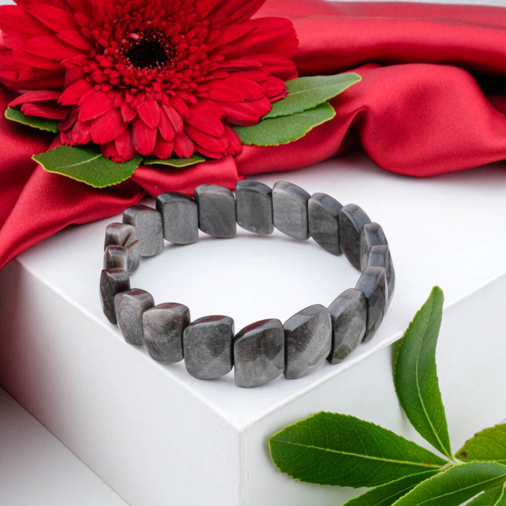 A Silver Sheen Obsidian bracelet with faceted, grey, tile-like beads in a Rolex-style design, on a white box.