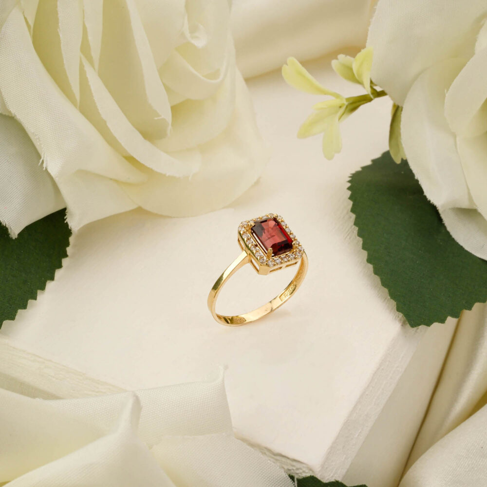 Custom oval garnet ring with halo setting in 14k yellow gold on white background