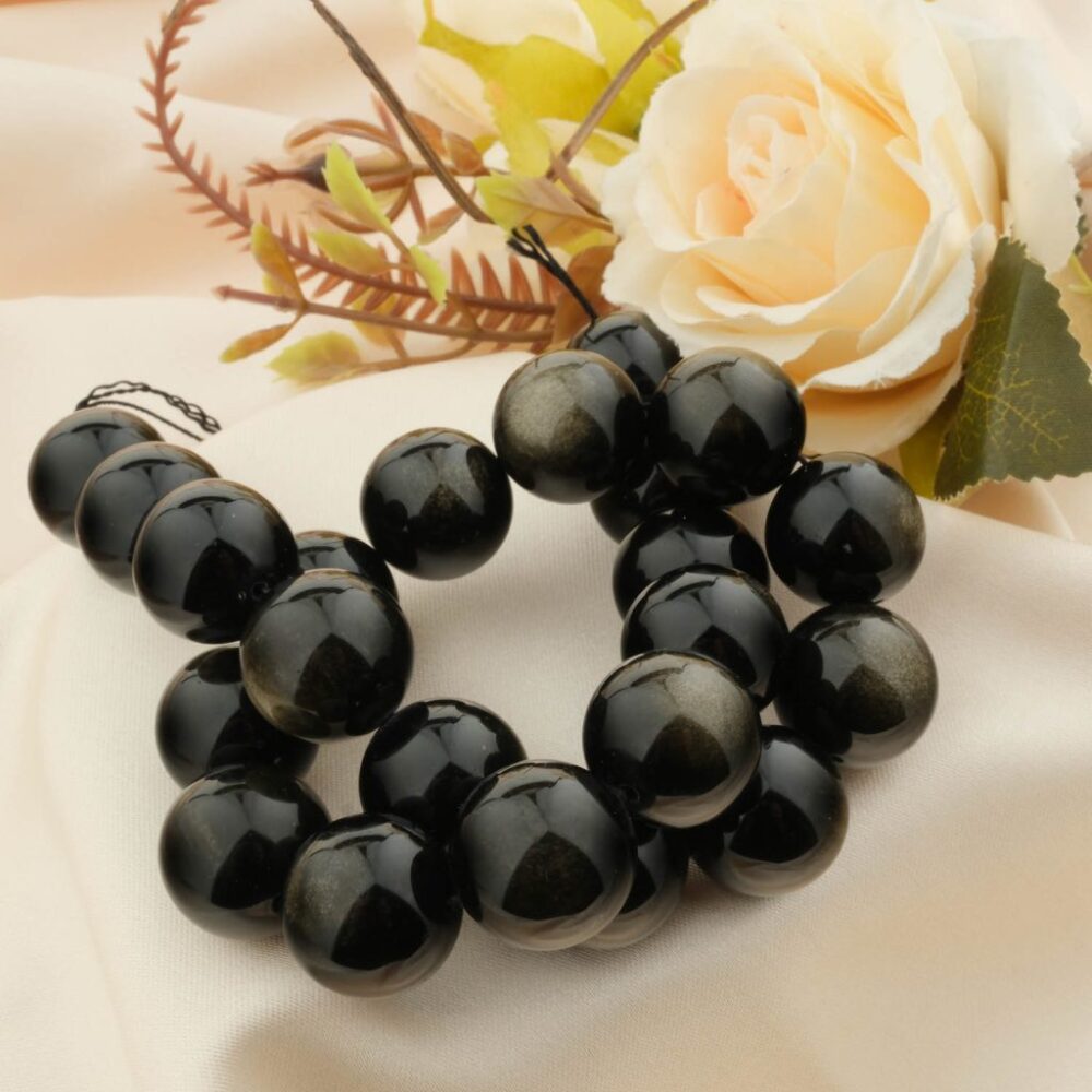 A 5A+ quality Gold Sheen Obsidian bracelet with large 18mm beads, styled on a cream satin cloth with a rose.