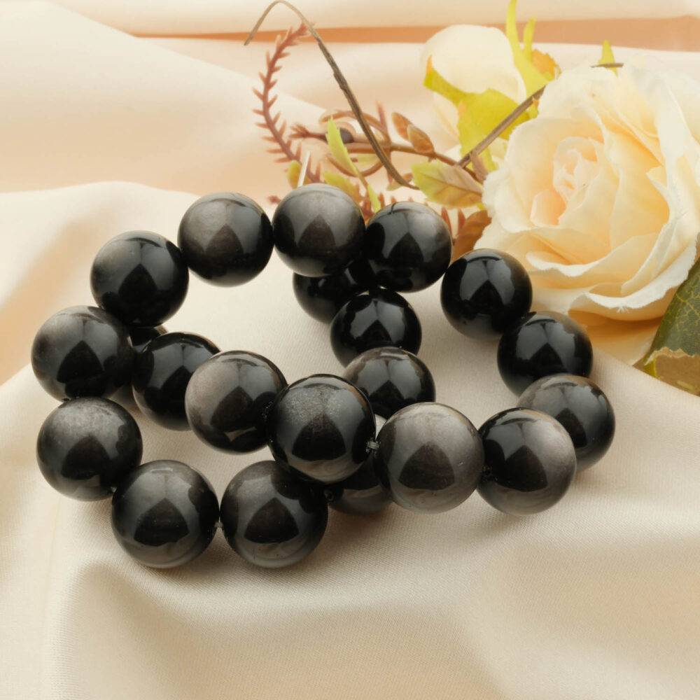 A 5A+ quality Silver Sheen Obsidian bracelet with large 18mm beads, styled on a cream satin cloth with a rose.