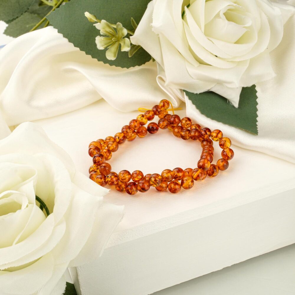 A strand of 6-6.5mm polished cognac amber beads on a white display