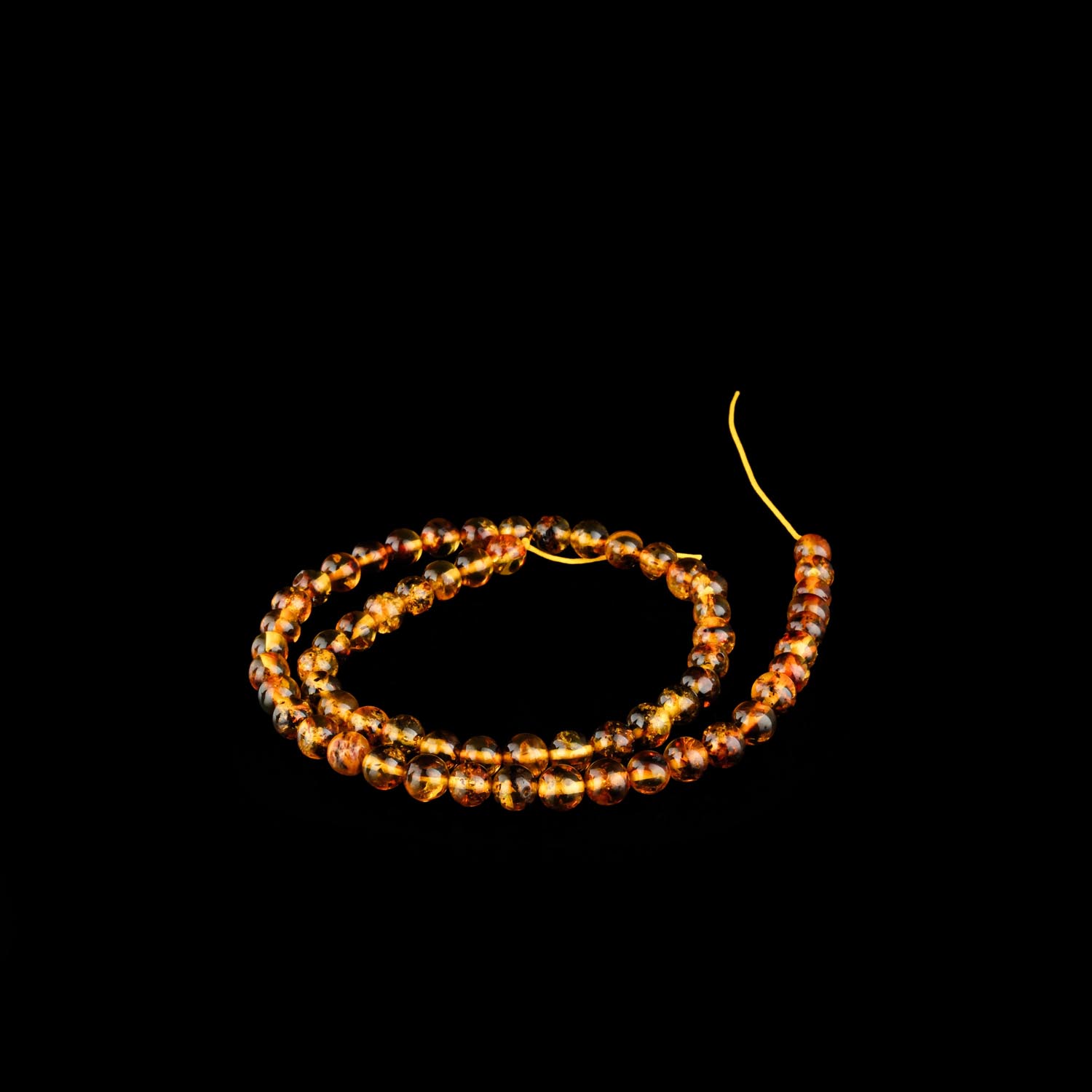 7mm-fosilli-kehribar-sap-dizi Ağ fonda tünd fosil daxil olan 7 mm cilalanmış konyak kəhrəba muncuqlar silsiləsi