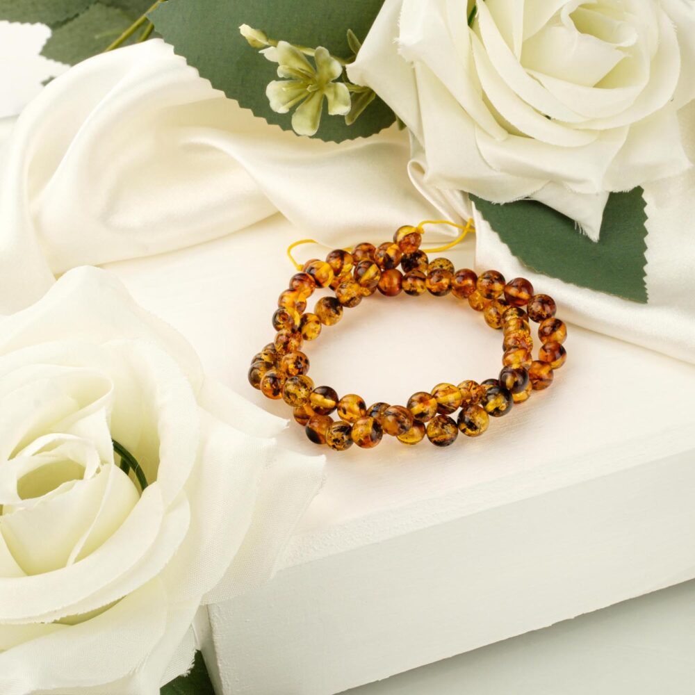 A strand of 7mm polished cognac amber beads with dark fossil inclusions on a white display