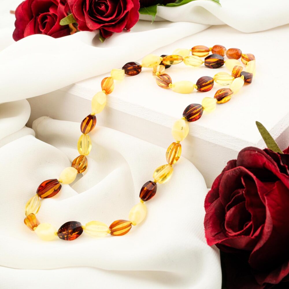 Certified original adult amber necklace with multi tone beads on white fabric and red roses
