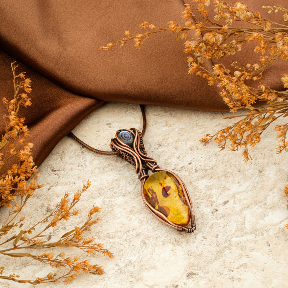 Handmade copper wire-wrap pendant with large golden amber and mother of pearl accent, on brown satin.