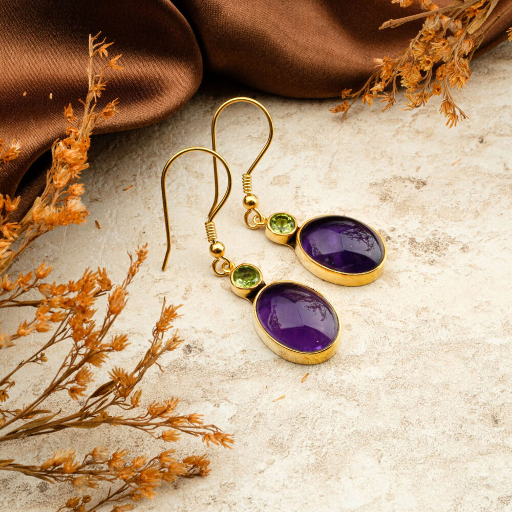 Premium Amethyst (oval cabochon) and Peridot (round) two-stone earrings in gold-plated 925 silver, on a brown background.