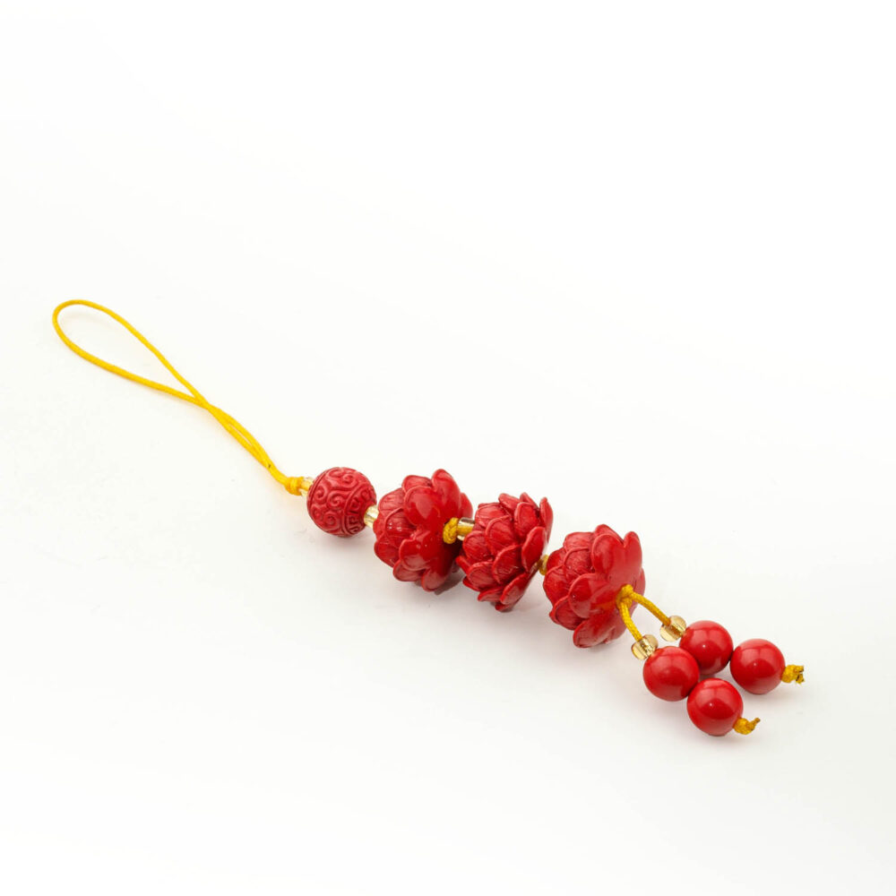 Amuleto de flor de loto de cinabrio rojo tallado con cordón amarillo, sobre superficie blanca y madera.