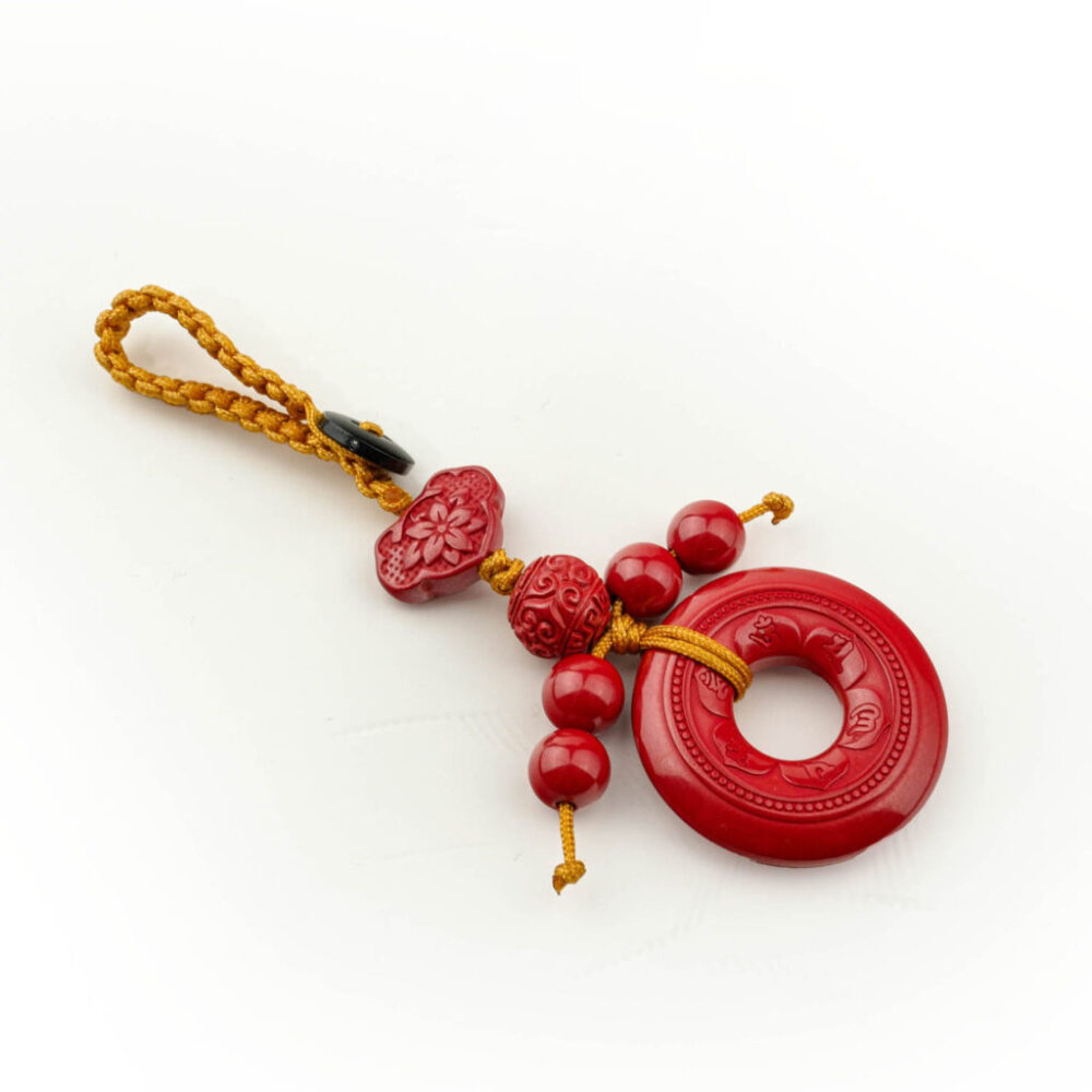 Amuleto Pi Disk de cinabrio rojo tallado con cordón amarillo, sobre superficie blanca y madera.