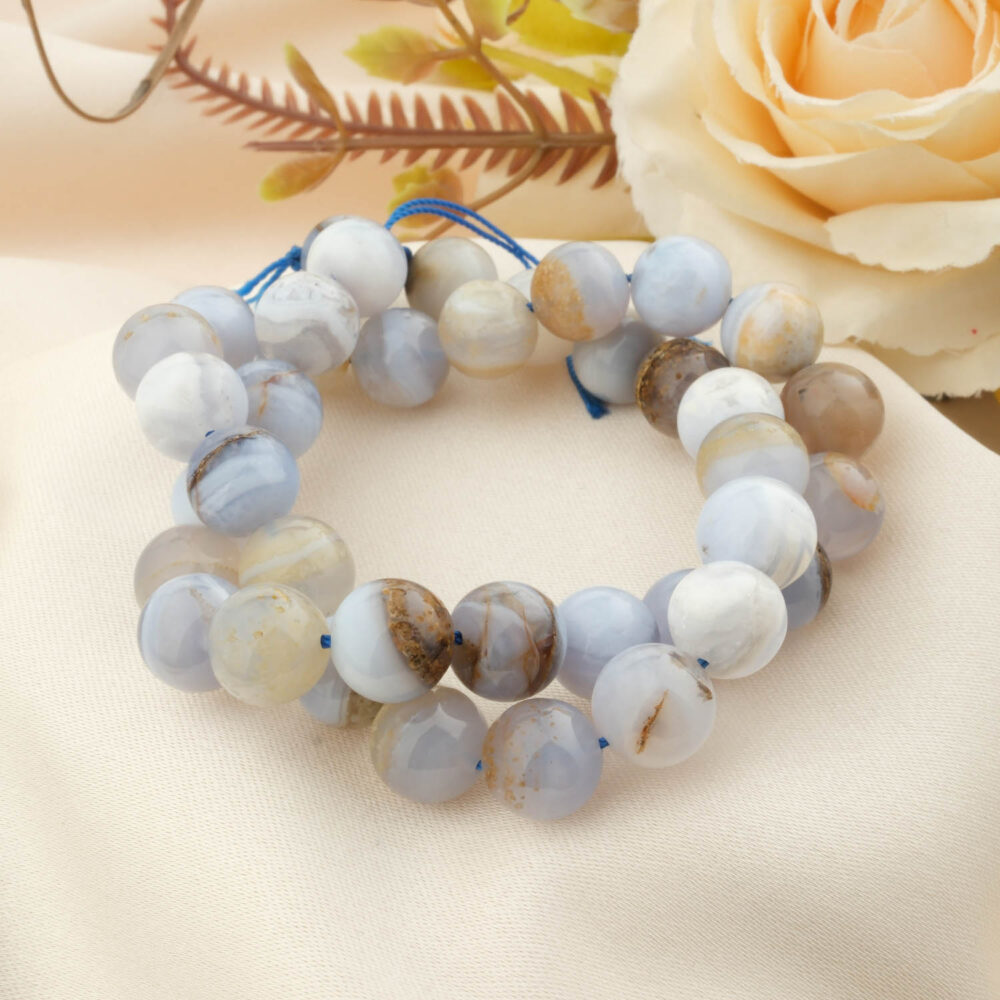 A strand of 5A grade 10mm round blue chalcedony beads, coiled on a cream silk background with a white rose.
