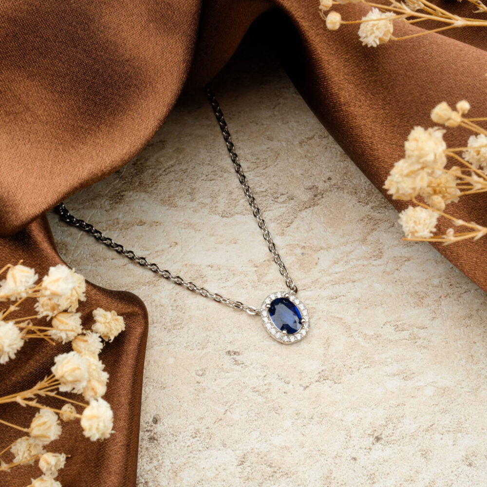 Premium Blue Sapphire halo necklace in 925 sterling silver on a brown satin background with dried flowers.