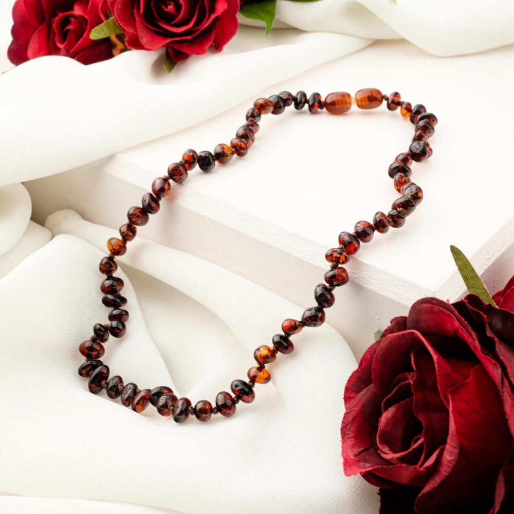 Certified original baby amber necklace with dark cognac beads on white background
