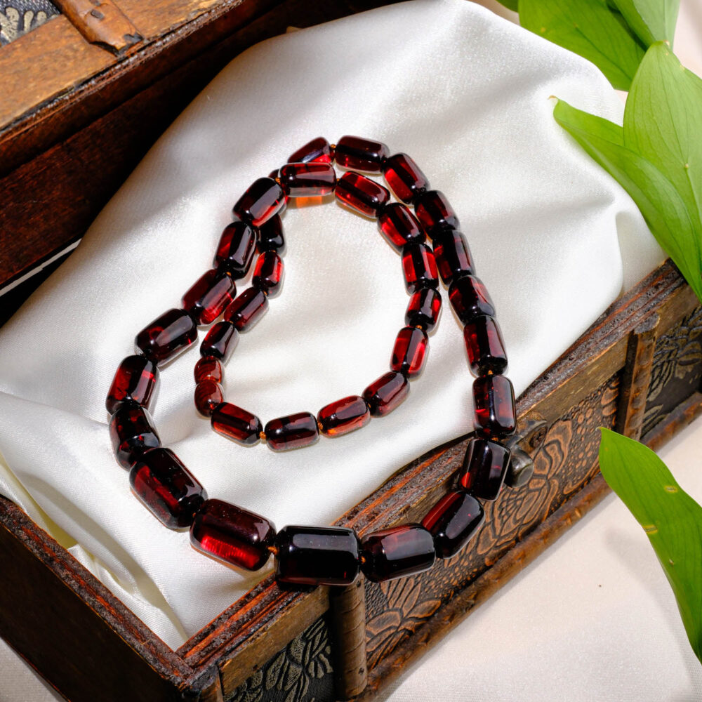 Certified genuine amber necklace with dark cherry capsule-shaped beads on white background