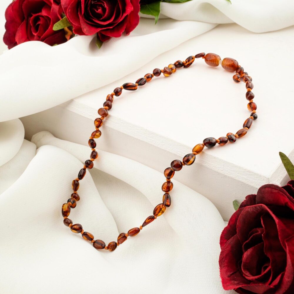 A certified Baltic Amber baby necklace with polished cognac baroque beads, on a white silk background.