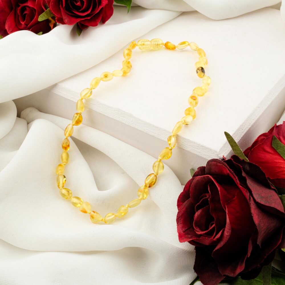 A certified Baltic Amber baby necklace with pale lemon-yellow baroque beads, displayed on a white silk background.