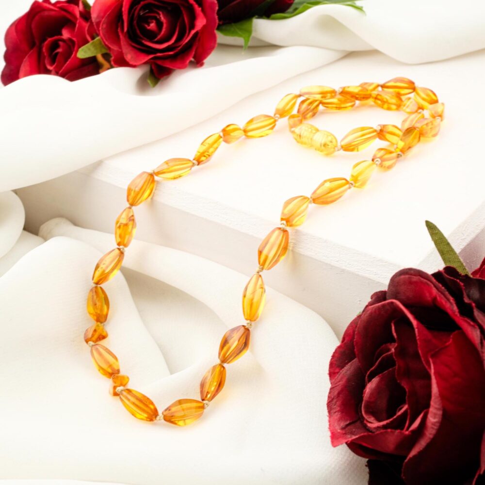 A certified Baltic Amber adult necklace with polished honey-cognac olive-shaped beads, styled on a white box with red roses.