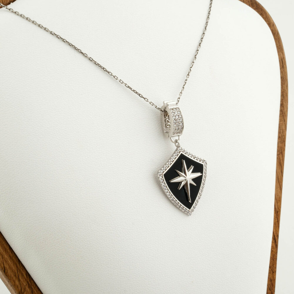 Collar premium de escudo Estrella del Norte en plata 925 con esmalte negro, sobre satén marrón.