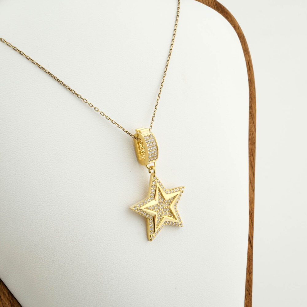 Collar premium de estrella en plata 925 chapada en oro, completamente cubierto de zirconitas, sobre satén marrón.