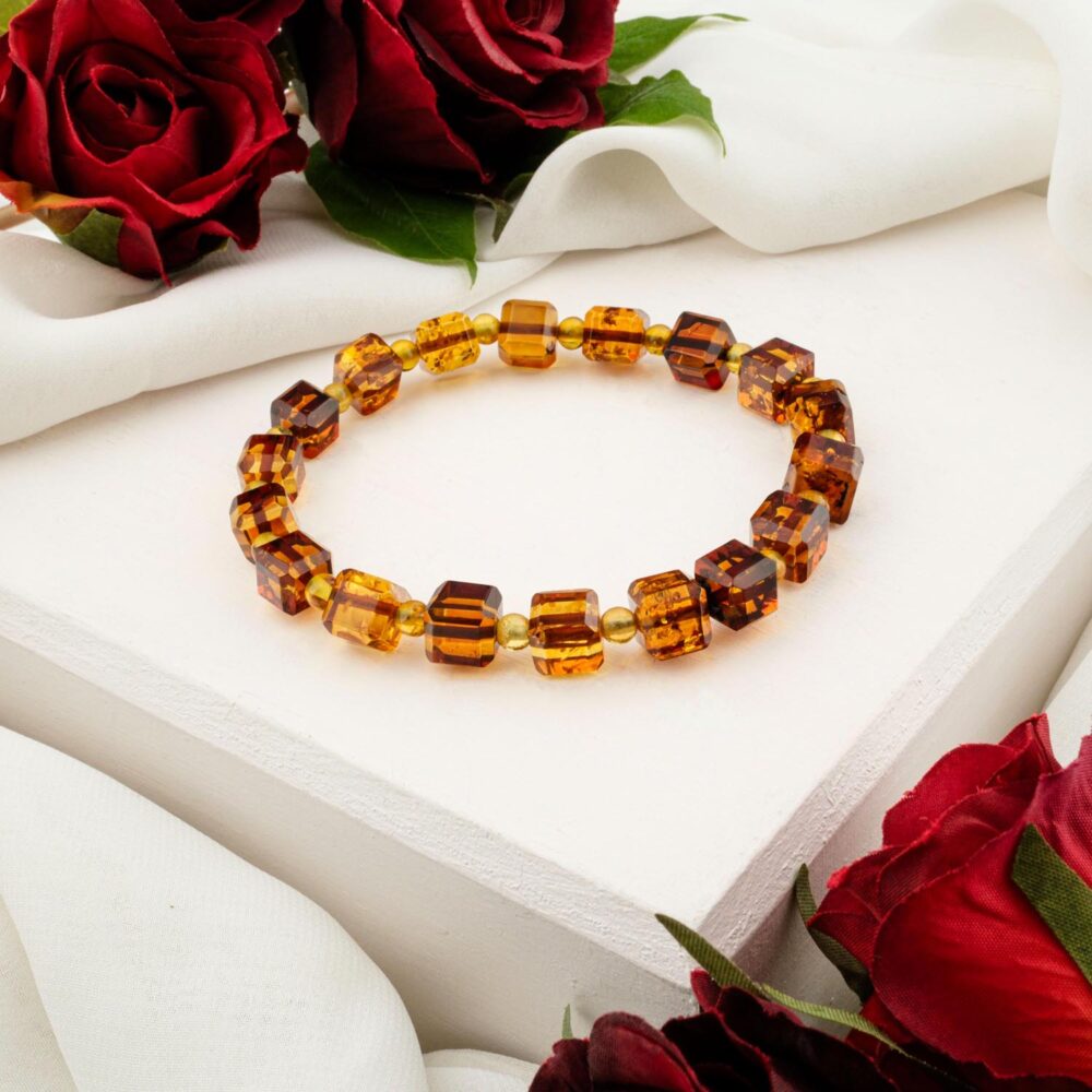 A multi-color Baltic Amber bracelet with faceted cube-cut beads (cognac/honey), styled on a white box with red roses.