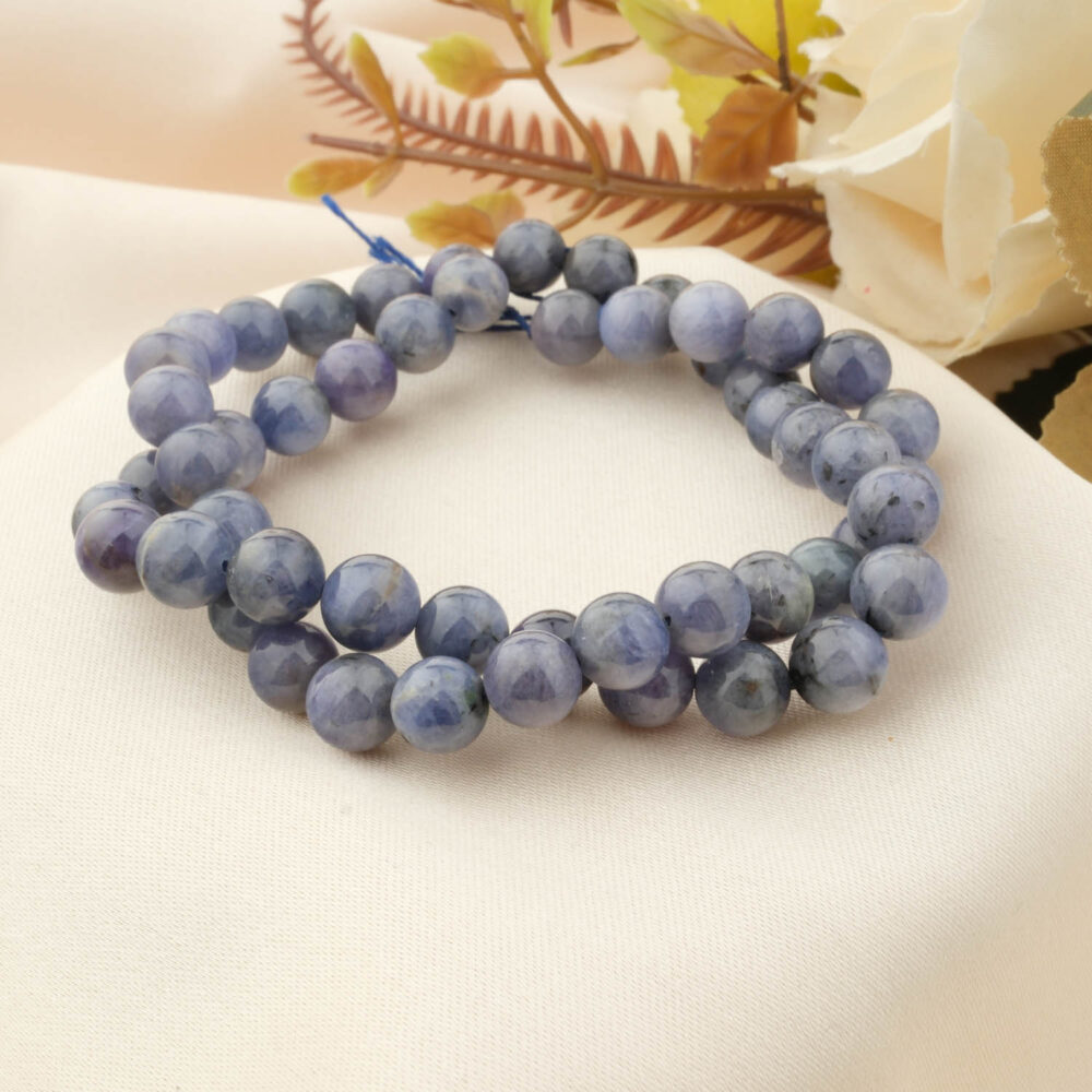A genuine faceted Tanzanite bracelet with 8mm beads, showing its violet-blue color on a cream satin cloth with a rose.