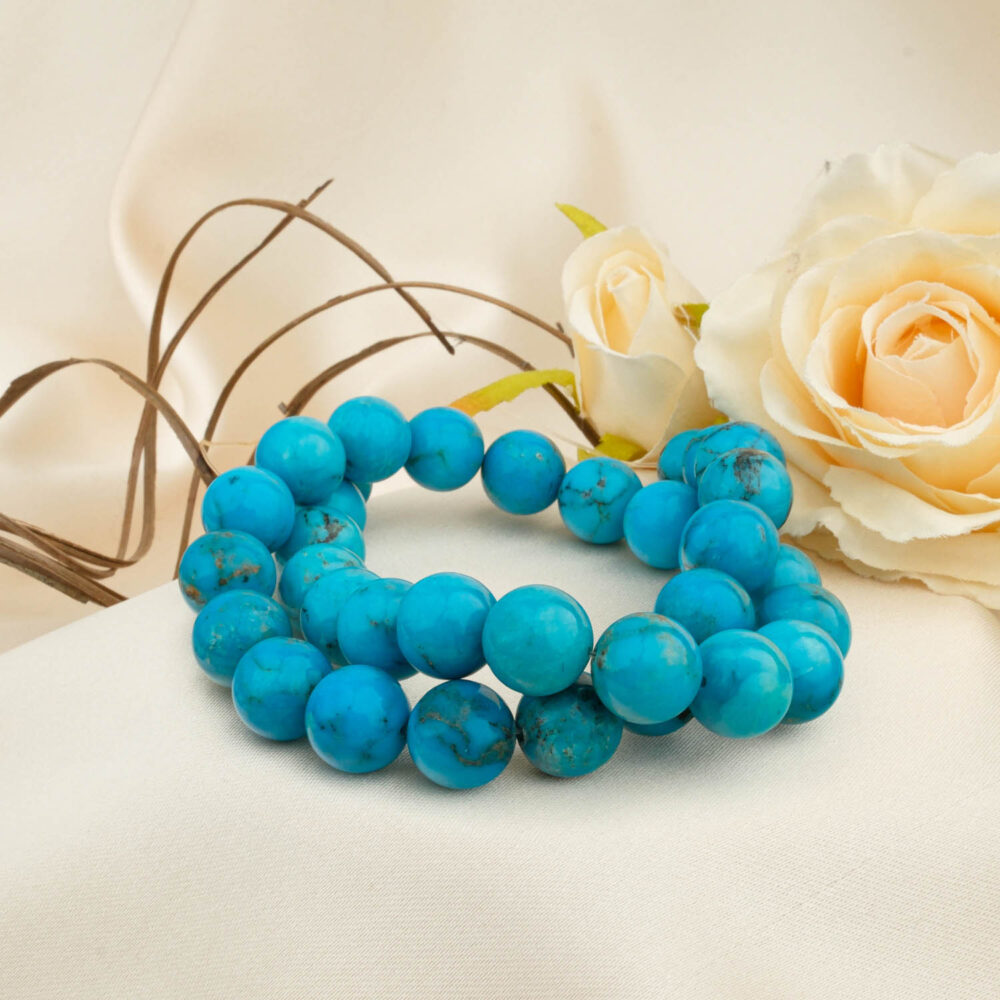 Fio de contas de Turquesa Grau 5A+ de 11-12mm com padrões de matriz natural em tecido creme com uma rosa.