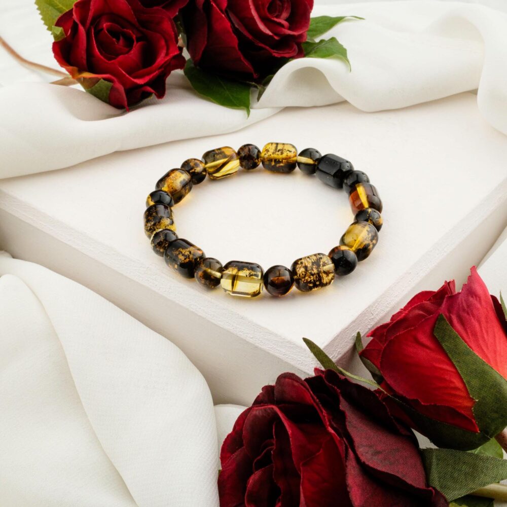 A multi-color "Forest Amber" bracelet with dark green, black, and yellow capsule-cut (cube) beads, styled on a white box with red roses.