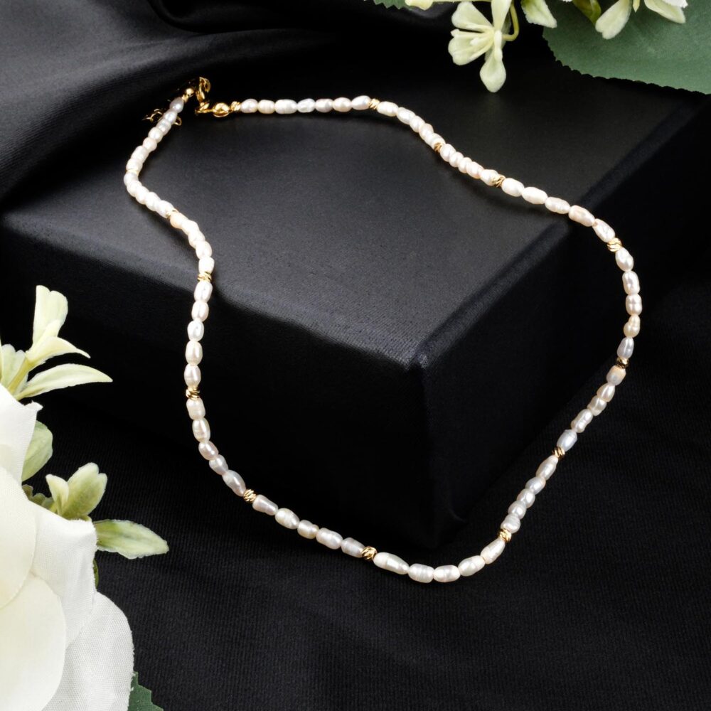 Delicate freshwater rice pearl necklace with gold-tone steel beads on black display