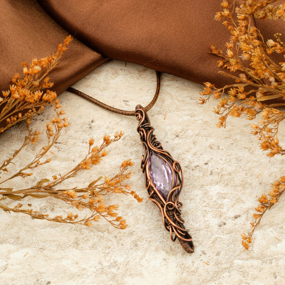 Handmade copper wire-wrap pendant with a large, faceted purple Amethyst stone, on a brown background.