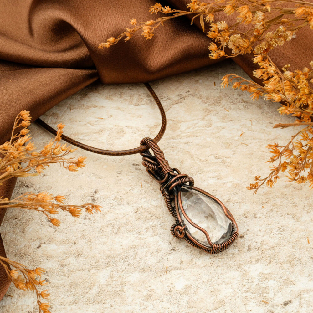 Handmade copper wire-wrap pendant with a large, clear faceted Najaf Stone (Clear Quartz) on a brown background.