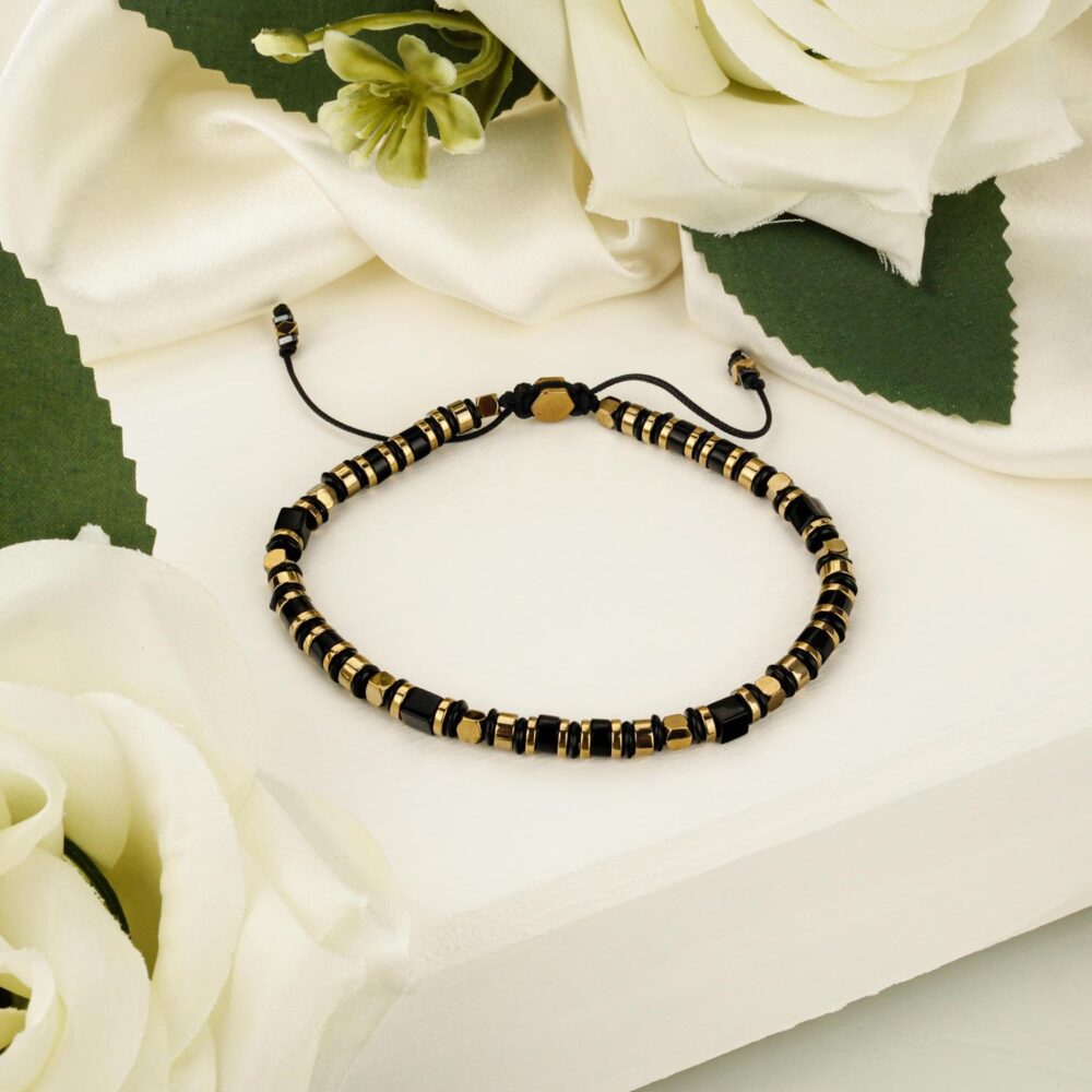 A sleek macramé bracelet featuring black onyx and gold-tone hematite geometric beads on an adjustable cord, displayed on a white surface.