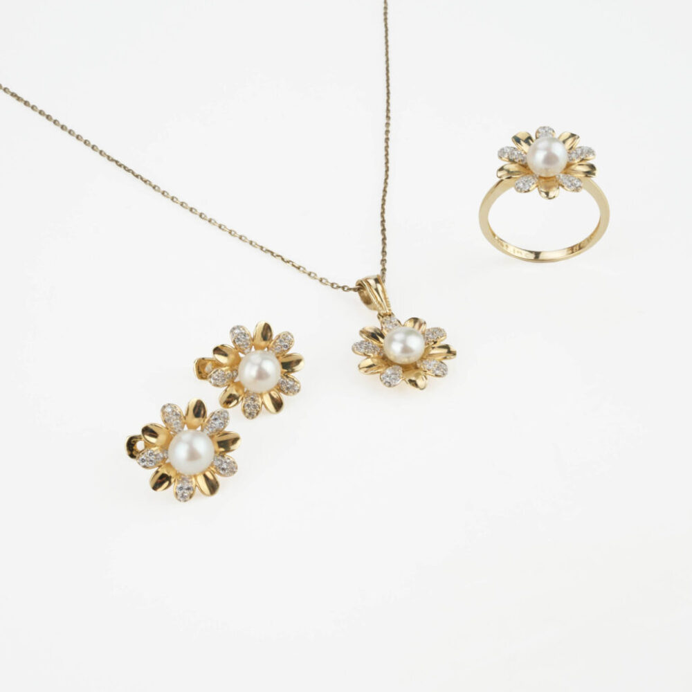 Modelo luciendo un juego completo de joyas de perlas y oro de 14k con halo: collar, pendientes y anillo.