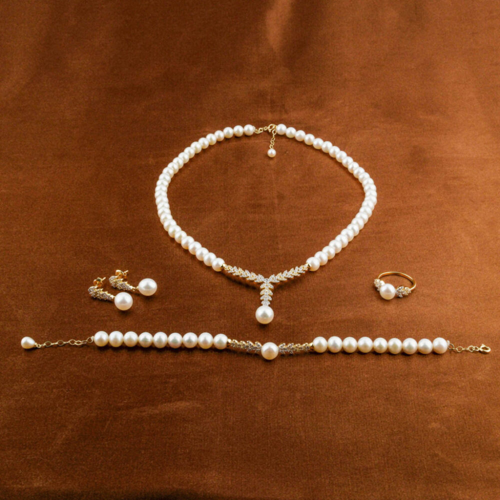 Modelo luciendo un juego completo de joyas de perlas y oro de 14k: collar, pendientes, pulsera y anillo.